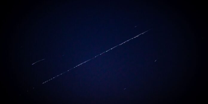 Diagonal light trail across a dark blue night sky from a long-exposure star trail photo.