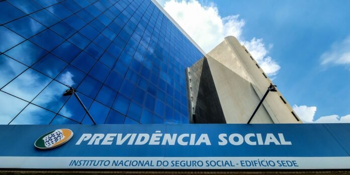 Modern blue-glass office building with a large sign reading Previdência Social above the entrance, under a clear sky.