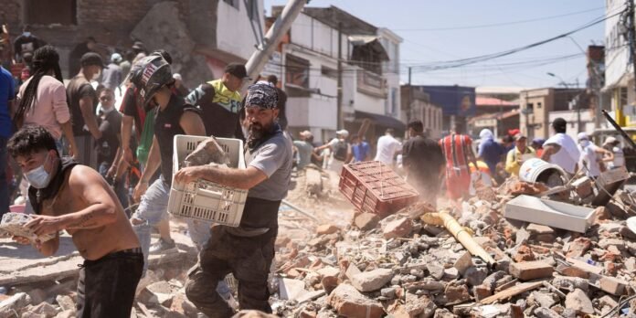 Crowd of volunteers clearing bricks and rubble after a building collapse, dust filling the street.