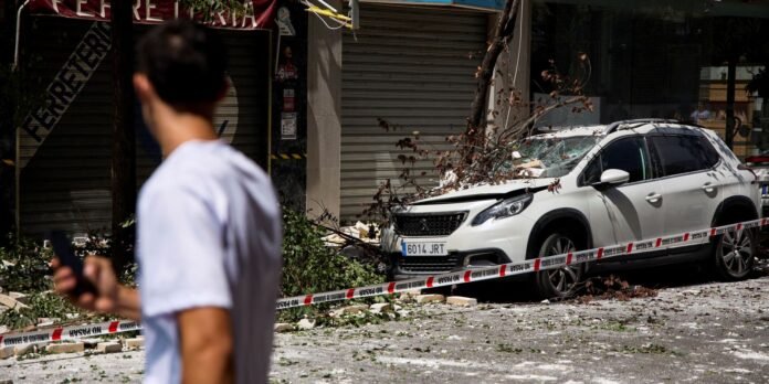 White SUV with front damage and fallen branches, taped off by police as a man in a white shirt walks past in the foreground.