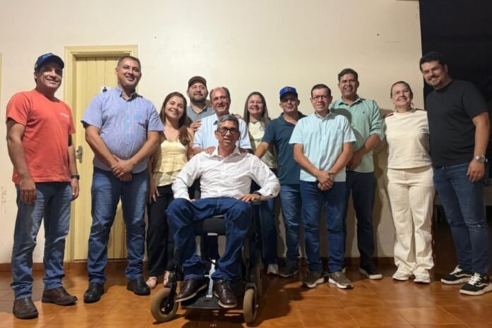 Group of adults posing indoors for a team photo, with a man in a wheelchair seated at center front.