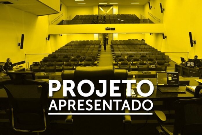 Empty lecture hall viewed from the presenter’s desk with two laptops; large text overlay reads 'PROJETO APRESENTADO'.