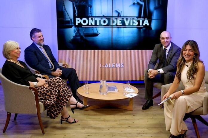 Four adults sit around a round coffee table on a TV set, with a large screen behind reading 'PONTO DE VISTA' and 'tv ALEMS' on the desk; a pitcher and glasses on the table.