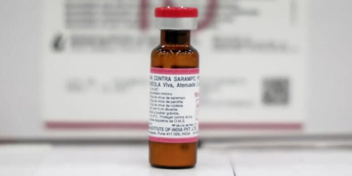 Brown medicine bottle with pink label and red cap on a white surface, in a lab setting (blurry background).
