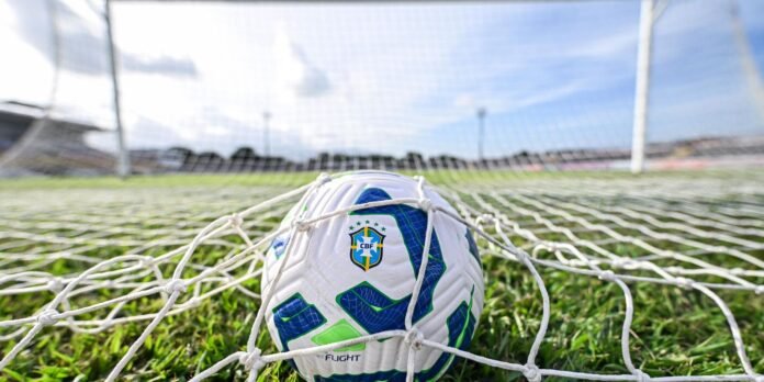 Close-up of a Brazil national team soccer ball wedged in a goal net on a grassy field.