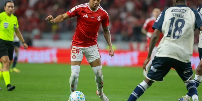 Soccer player in red jersey (number 28) dribbling the ball on a green field during a match.