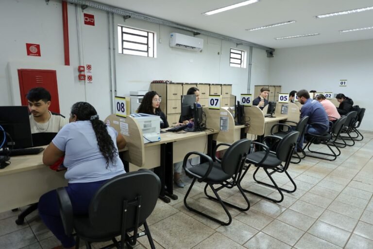 People seated at computer desks in a row, each at a numbered workstation in a service center or call center.