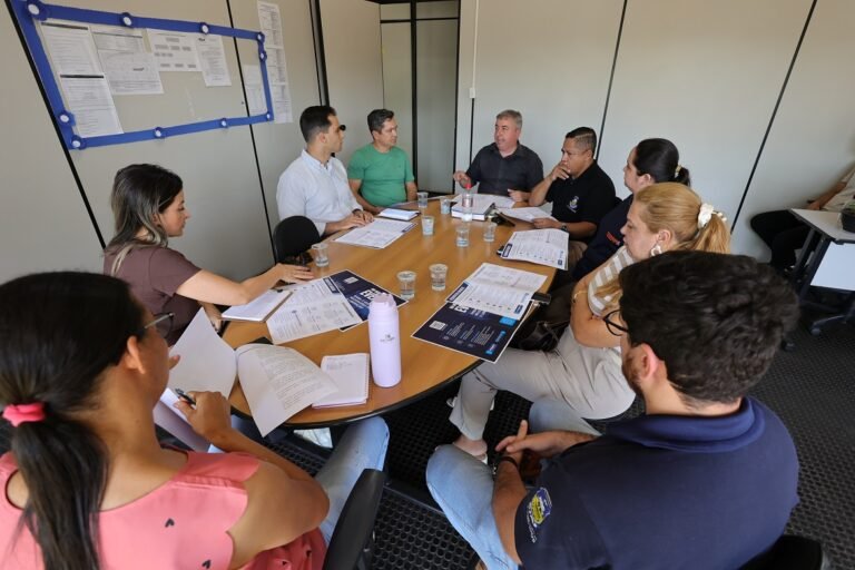 Group of nine people around a conference table in a bright meeting room, reviewing documents and notes together.