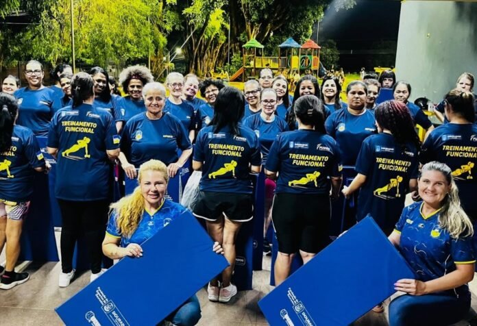 Group of people in matching blue shirts at an outdoor functional training event, two women in front holding large blue boards.