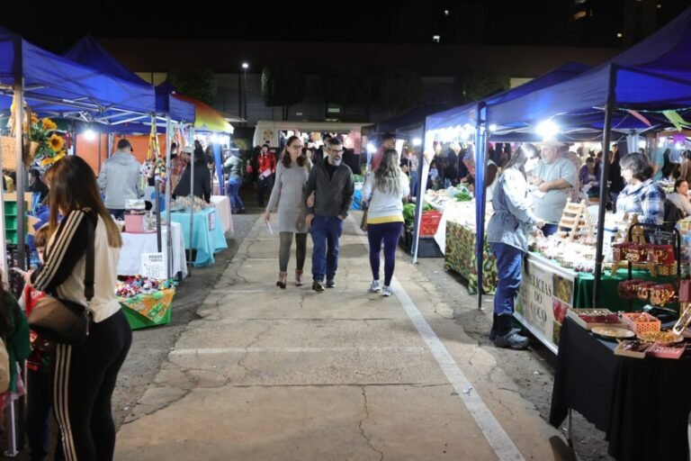 Night market at night with blue canopied stalls and shoppers browsing colorful goods along a cracked pavement road.
