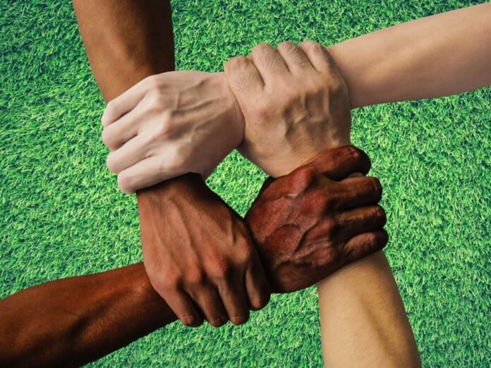 Diverse hands clasped in a circle on a green grass background, symbolizing teamwork and unity beneath their joined grips.