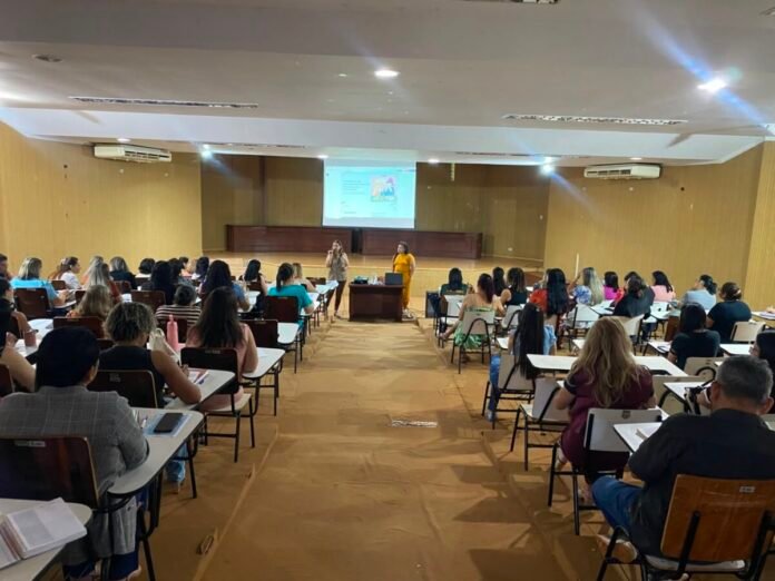 Large lecture hall with two presenters at the front addressing a full audience of students and a projected slide on the screen behind them