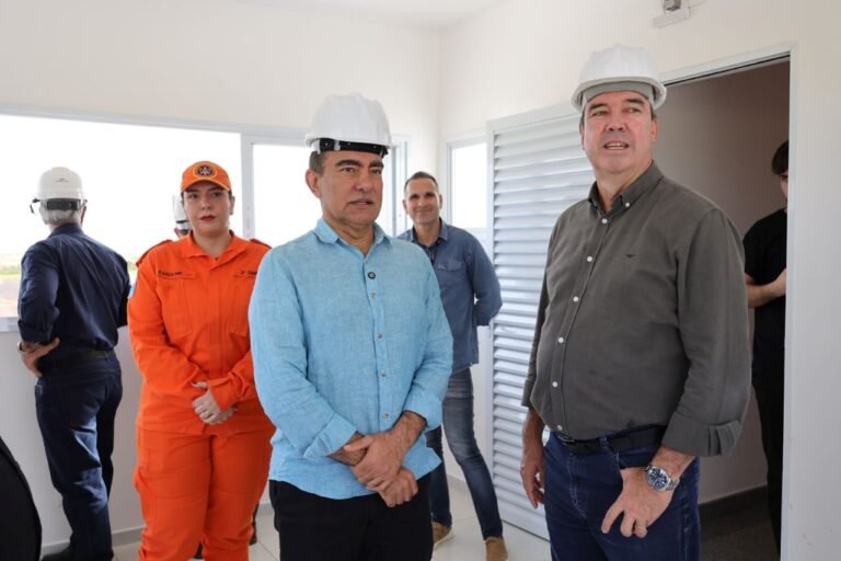 A group of construction workers wearing hard hats indoors, including a man in a blue shirt and a woman in orange coveralls, looking toward the camera.