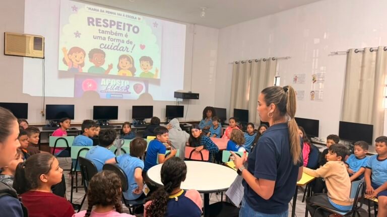 Teacher explains a lesson to a diverse group of children seated around tables as a slide reads 'RESPEITO também é uma forma de cuidar'.