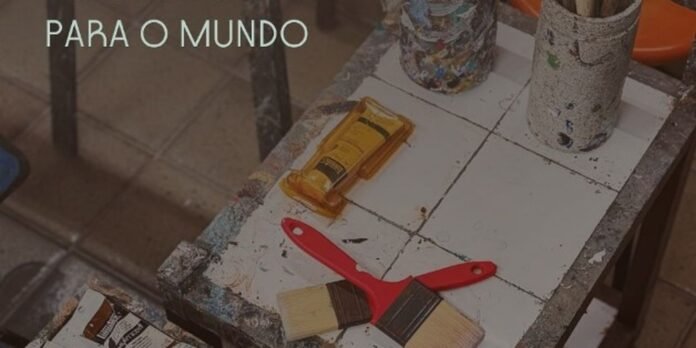 Art studio workspace with paint tubes, brushes, and a red spatula on a paint-splattered table; overlay text 'PARA O MUNDO'.