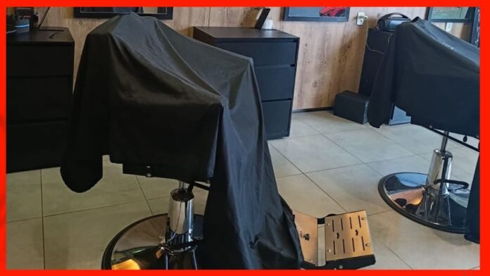 Barber shop interior with two black chairs covered by cloths and a tiled floor surface.