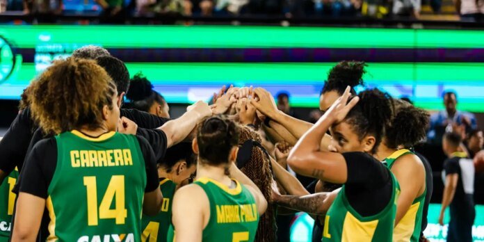 Basketball players in green uniforms huddle in a circle, hands joined in the center before a game.