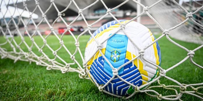 Soccer ball with Brazil crest wedged in the net of a goal on a green field
