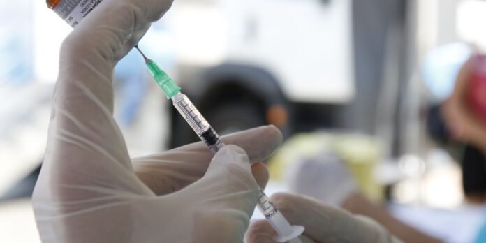 Gloved hands preparing a syringe with a vaccine vial in a clinical setting, ready for injection.