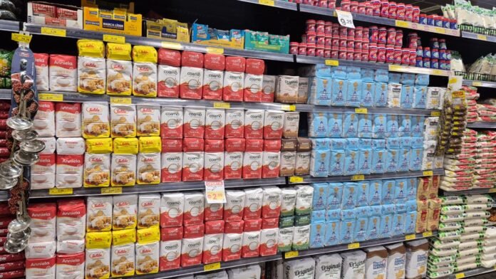 Aisle in a supermarket with neatly stacked bags of flour on metal shelves.