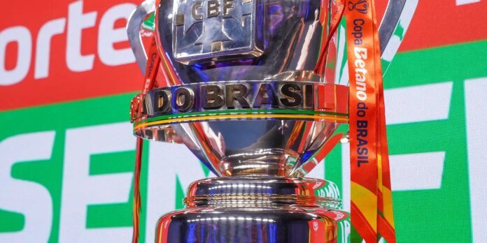 Brazil Cup trophy close-up with metallic letters reading BRASIL and red ribbons in a vibrant stadium backdrop