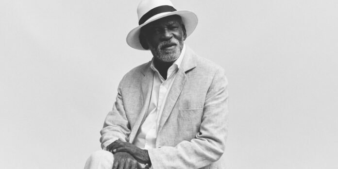 Black-and-white portrait of an older man in a light blazer and fedora, looking thoughtful.