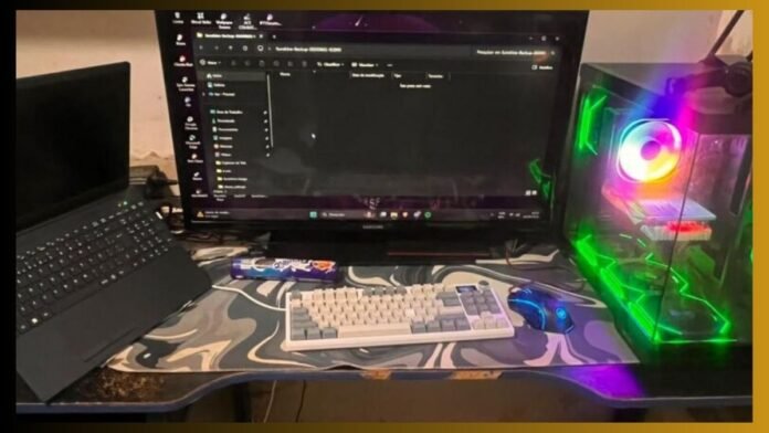 Modern computer workstation: laptop on the left, large monitor in the center, keyboard and mouse on a camo-pattern desk mat, and RGB-lit desktop tower on the right with a visible side panel glow.