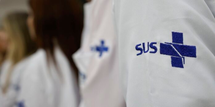 Close-up of a white lab coat with a blue cross logo and the letters SUS embroidered on the chest area.