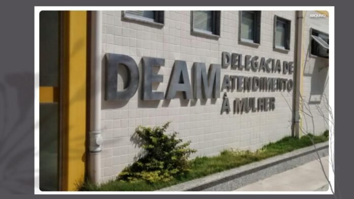 Exterior wall with large 3D sign reading 'DEAM Delegacia de Atendimento à Mulher' on a white tiled surface, with a sidewalk and small plants in front.