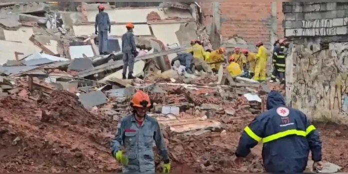 Emergency responders in helmets and protective gear search rubble at a collapsed building site with bricks and concrete scattered around.