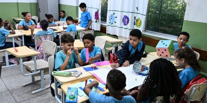 Group of students in blue uniforms work on a paper craft at shared desks in a bright classroom.