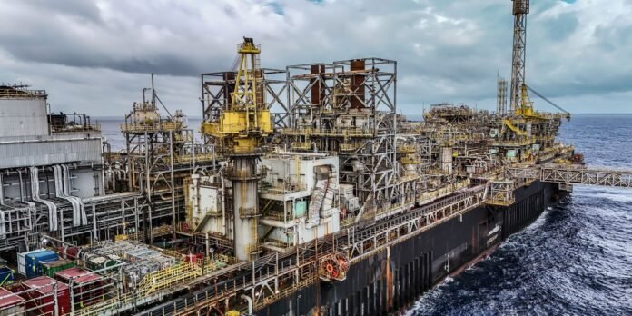 Offshore oil rig vessel with yellow cranes and complex metal framework beside the sea.