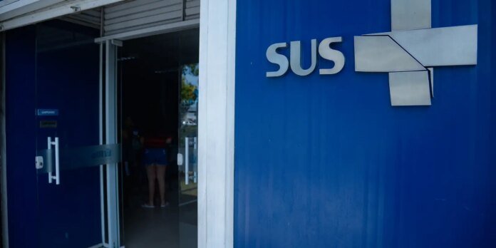 Blue exterior wall with a silver SUS logo and geometric shapes next to a glass door entrance to a building.