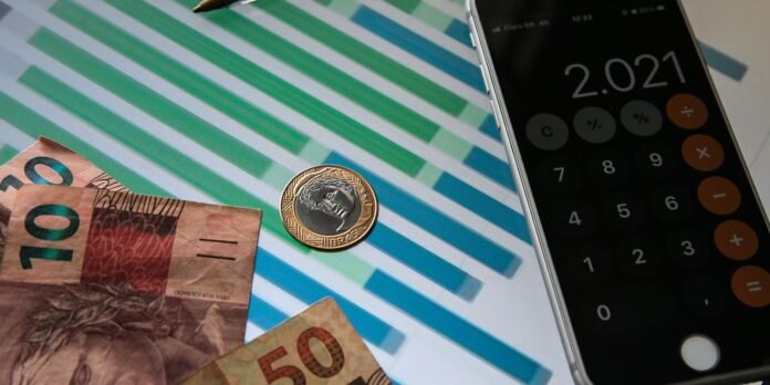 Brazilian money (100 and 50 reais) with a coin and a smartphone calculator displaying 2.021.