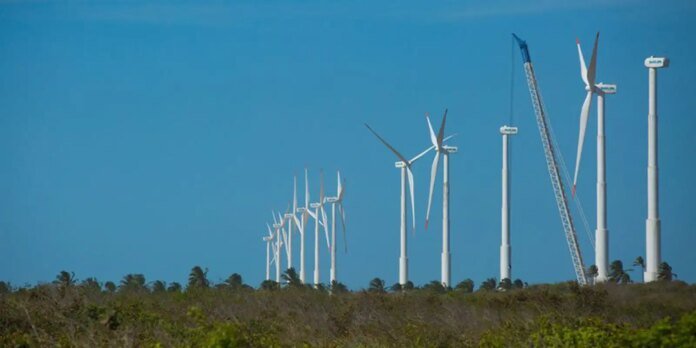Row of wind turbines on a flat grassy landscape under a clear blue sky, with a crane nearby during installation.