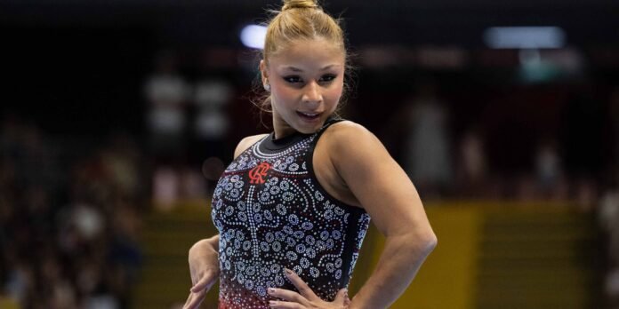 Female gymnast in a sparkling black rhinestone leotard posing with hands on hips in an arena.
