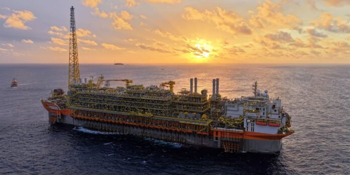 Large offshore oil rig floating at sea during sunset with orange and yellow sky and calm water horizon nearby