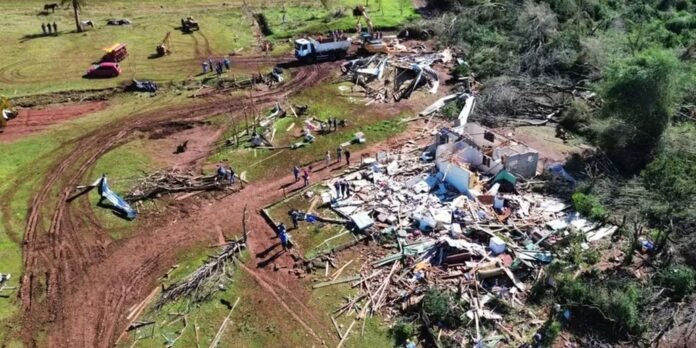 Aerial view of a rural disaster site with a collapsed building, scattered lumber, and rescue crews inspecting the debris area
