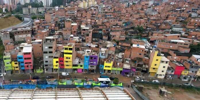 Row of brightly painted houses along a hillside favela with brown brick buildings behind.