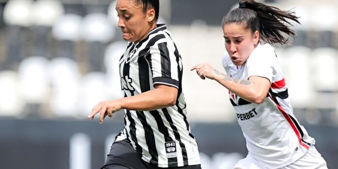 Two female soccer players sprint side by side during a match, one in a black-and-white striped kit and the other in white with red and black accents.