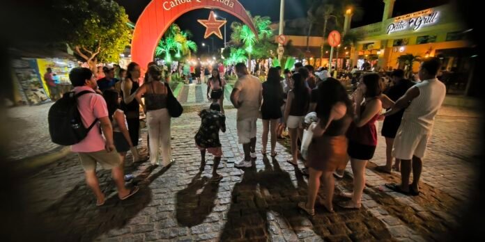 Crowd of people gathered on a cobblestone street at night around a performer beneath a red arch and star lights.