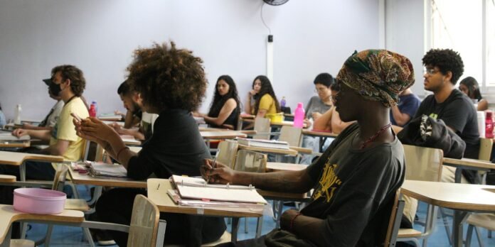 Students in a classroom, some taking notes at desks during a lecture.
