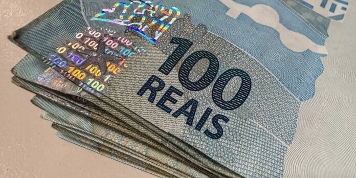 Stack of Brazilian 100 reais banknotes fanned out, blue with '100 REAIS' and holographic security strip