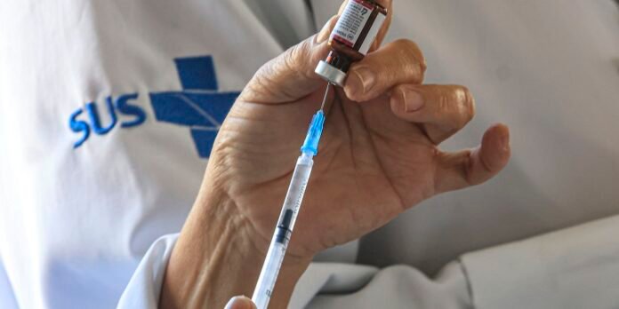 Medical professional's hand drawing liquid from a vial into a syringe, preparing an injection.