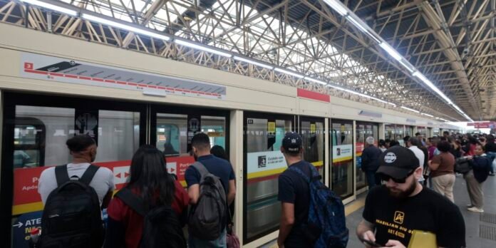 Crowded urban subway platform with passengers boarding a beige metro train under a metal framework roof.