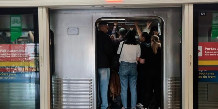 Crowded subway carriage doorway with passengers standing and gripping overhead rails while entering or exiting the train.