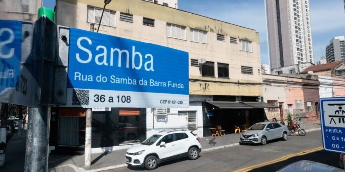 Bright blue Samba sign on a busy urban street; a white car is parked at the curb with buildings in the background.