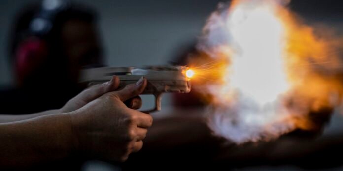 Person firing a handgun, bright muzzle flash and smoke in a dim room.