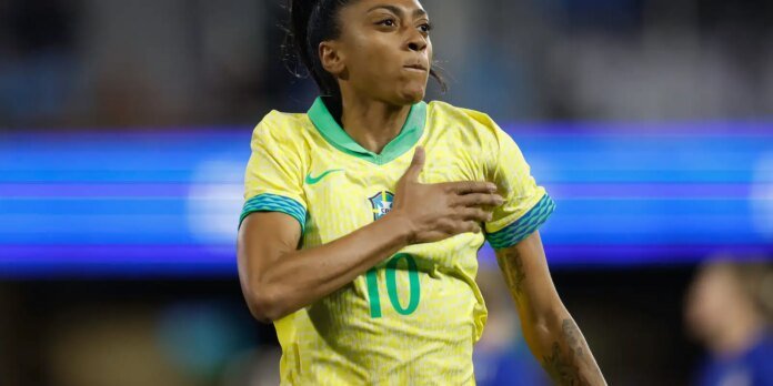 Brazilian female soccer player in a yellow Brazil kit with green trim, hand over chest in celebration during a match, wearing number 10