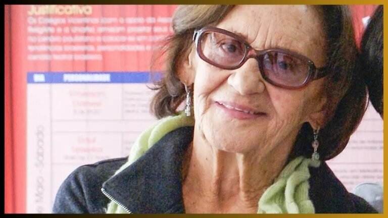 Older woman with short brown hair and glasses, wearing a green scarf and dark jacket, smiling at the camera.